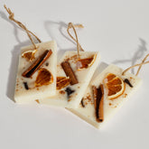 Three rectangular soy wax melt decorations with citrus peel and cinnamon sticks embedded, hanging from twine.